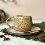 Le mug COUMBA en céramique artisanale sur une table avec sa sous-tasse ASMA.