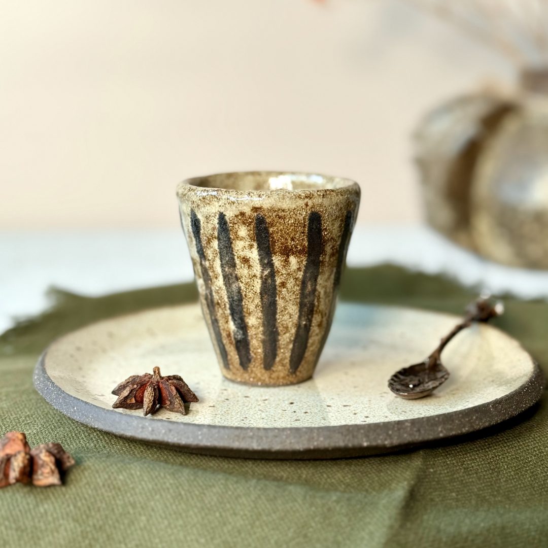 La tasse NAIA avec la sous-tasse en céramique artisanale sur une table.