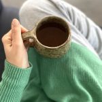 Vue de dessus d'une personne assise sur un canapé tenant entre ses mains le mug Coumba en grès artisanal.