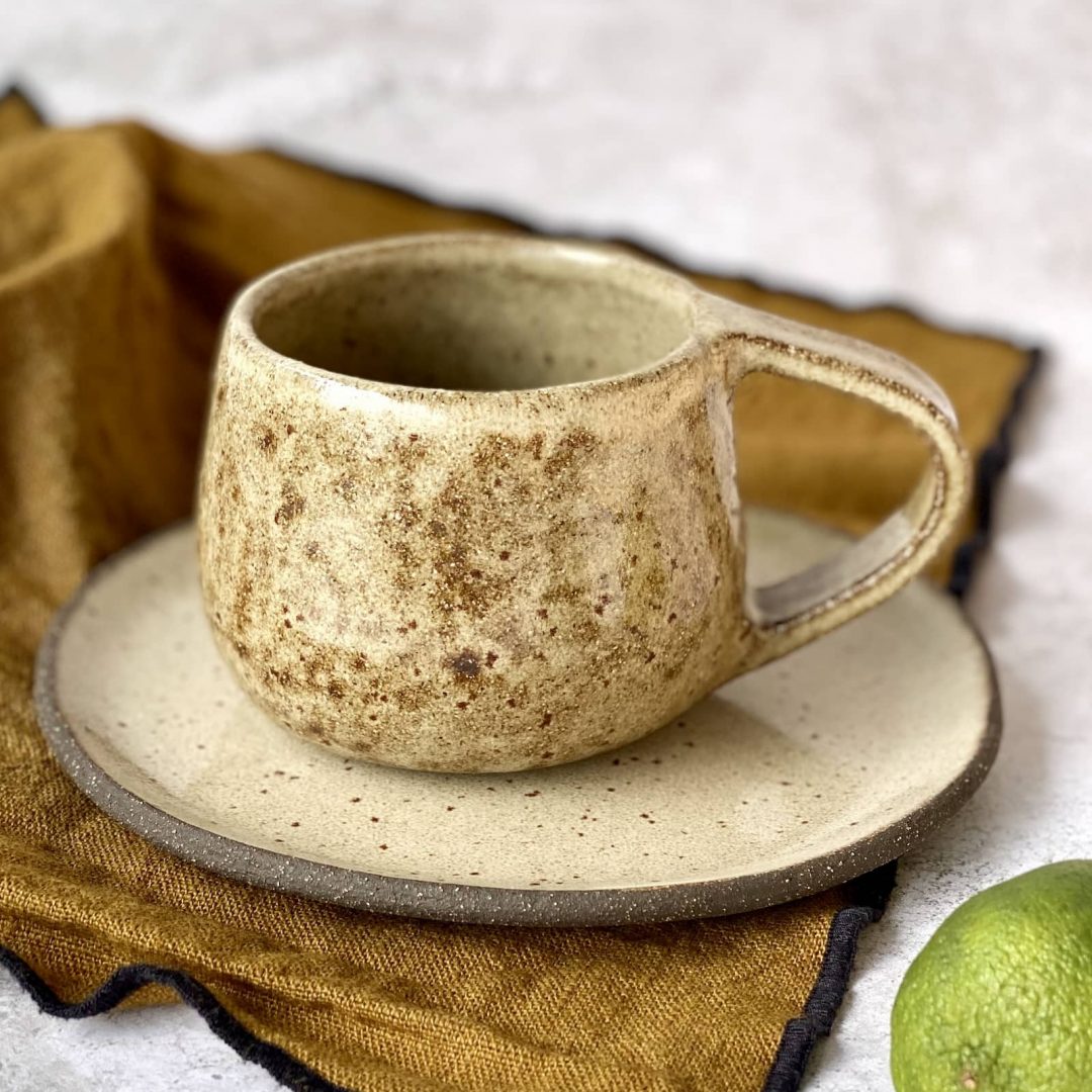 Mug coumba en grès artisanal posé sur sa sous-tasse asma, sur une table avec nappe.