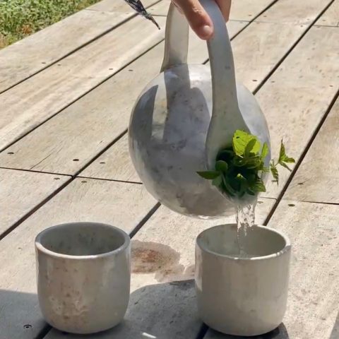 Carafe en céramique artisanale versant de l'eau dans une tasse Astral en grès.