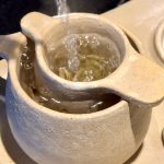 Thé versé dans l'infuseur du set à thé RIKU, posé sur son plateau en céramique artisanale en grès.