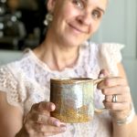 Mug GARANCE en grès artisanal tenu entre les mains, avec la céramiste floue en arrière-plan.