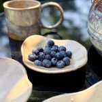 Coupelle MILA en grès artisanal au premier plan, accompagnée de l'assiette LINA et du mug GARANCE en arrière-plan sur une table dressée.