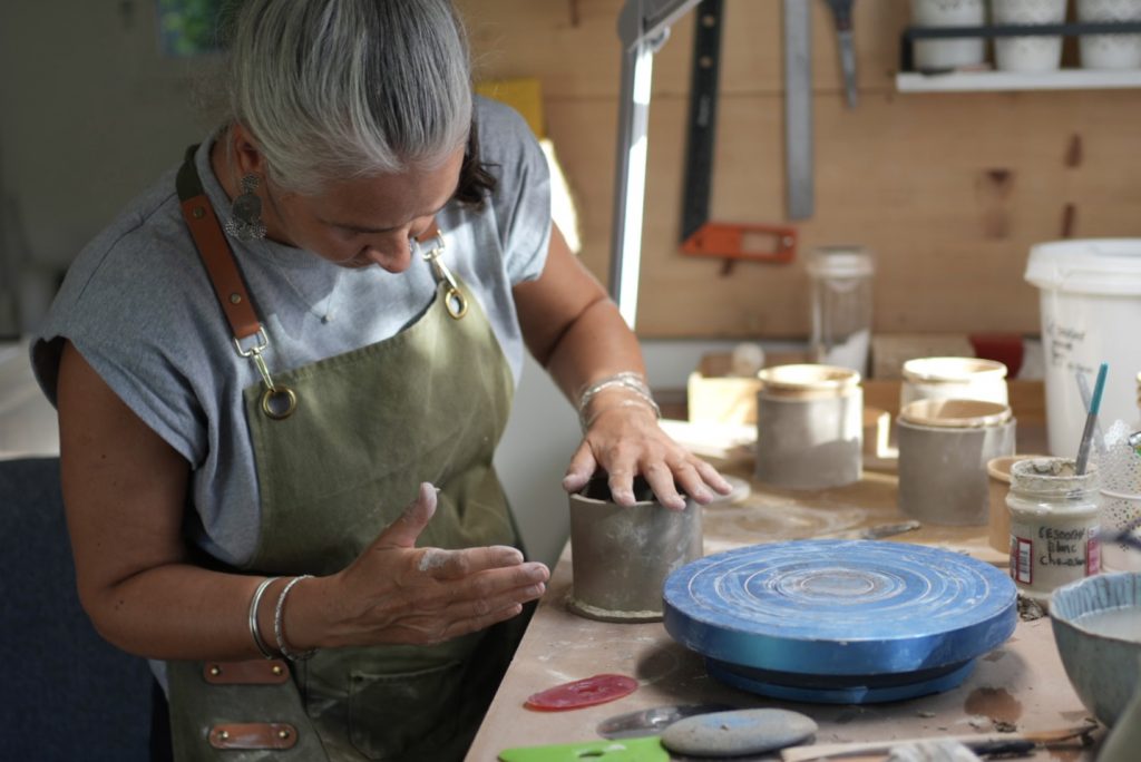 Lis céramiste façonnant une tasse en grès dans son atelier céramique artisanale, avec plusieurs tasses en arrière-plan.