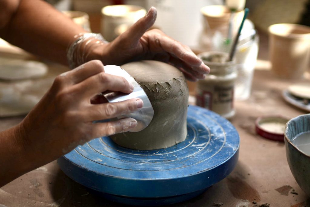 Gros plan sur les mains de Lis céramiste, peaufine une tasse en grès avec une estèque dans son atelier de céramique artisanale.