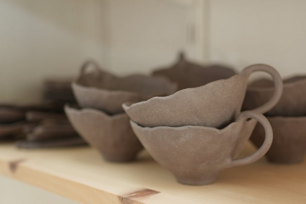 Tasses en grès noir de céramique artisanale posées sur une étagère dans l'atelier.