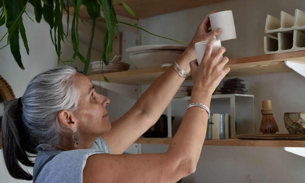 Lis céramiste rangeant deux tasses en grès dans son atelier de céramique artisanale.