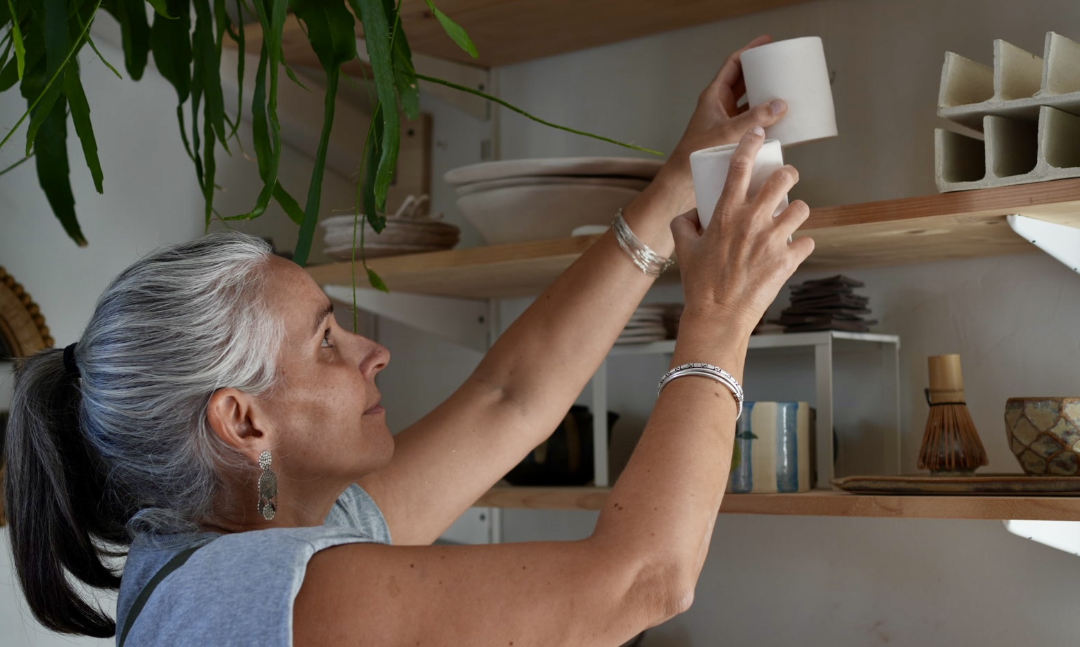 Lis céramiste rangeant deux tasses en grès dans son atelier de céramique artisanale.