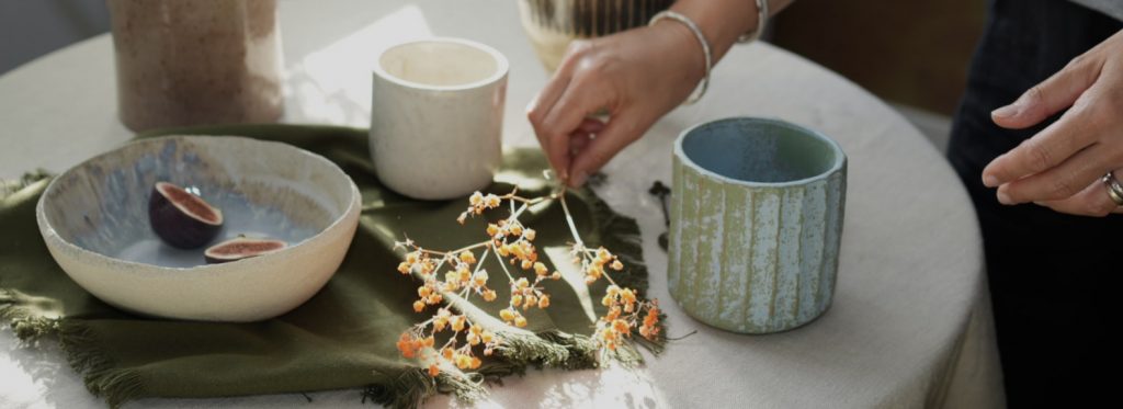 Table dressée dans la salle à manger avec la collection de vaisselle en grès artisanal faites main de LIS Céramique : tasse ASTRAL, mug KAITO et bol AURORA. Des mains déposent des fleurs pour un moment de convivialité.