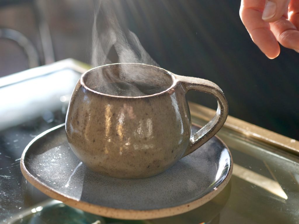 Un mug en céramique artisanale avec un thé chaud fumant sur une sous-tasse.