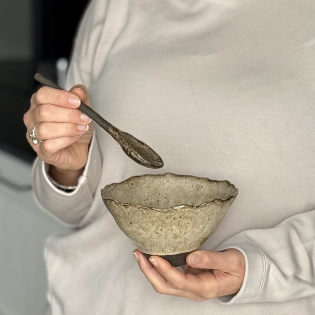 Lis Céramiste tient le bol Camellia dans une main et de l'autre main la cuillère bintou en céramique artisanale.
