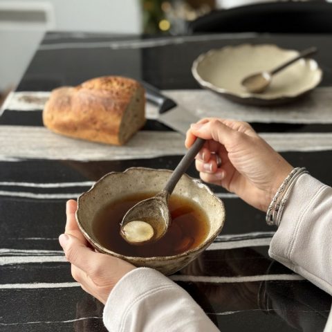 Bol camellia en grès avec bouillon, servi à la main avec la cuillère bintou, pain et assiette Jasmina en arrière-plan.