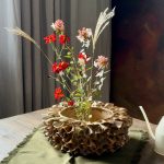 Vase ÉMILE en céramique artisanale posé sur une table, avec des fleurs piquées dans son dôme, en situation dans une salle à manger.