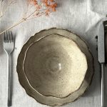 Bol Camellia en grès noir posé sur l’assiette Jasmina en céramique artisanale vus de dessus, avec une fourchette à gauche et un couteau à droite dans une mise en scène sur table.