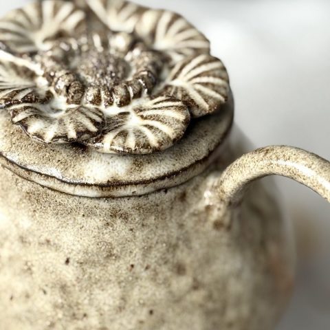 Gros plan sur le couvercle sculpté de la théière Cosmos avec un détail de la anse, en grès noir émaillé crème.