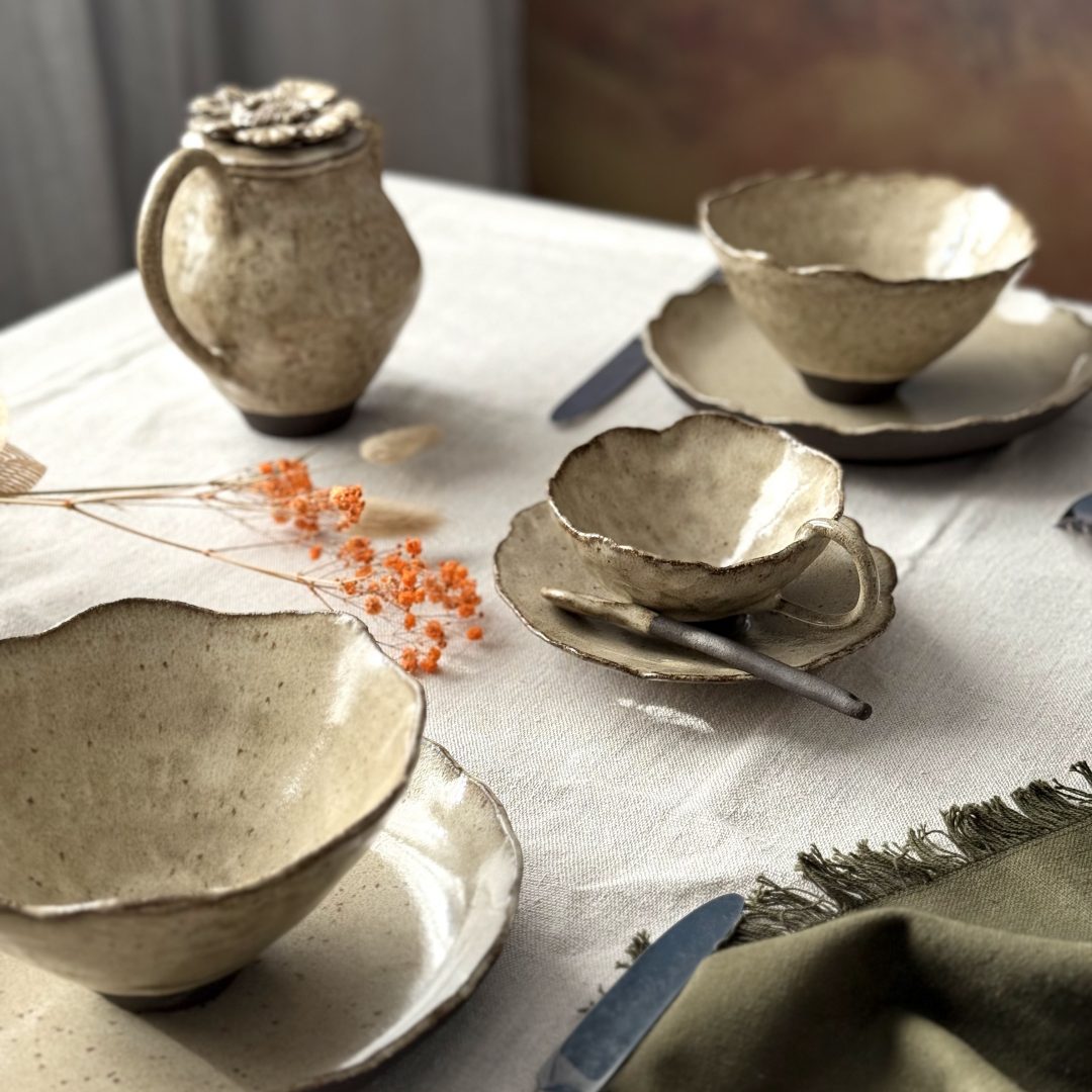 Vaisselle artisanale en grès de la collection FLOR dressée sur une table : théière cosmos, tasse Lilium, sous-tasse Dahlia, cuillère Rosa, bol Camellia et assiette Jasmina.