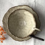 Vue rapprochée de la tasse Lilium posée sur la sous-tasse Dahlia, avec la cuillère Rosa placée dessus, photographiée depuis le dessus.