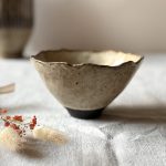 Bol Camellia en grès noir émaillé crème, vue de profil et posée sur une table.