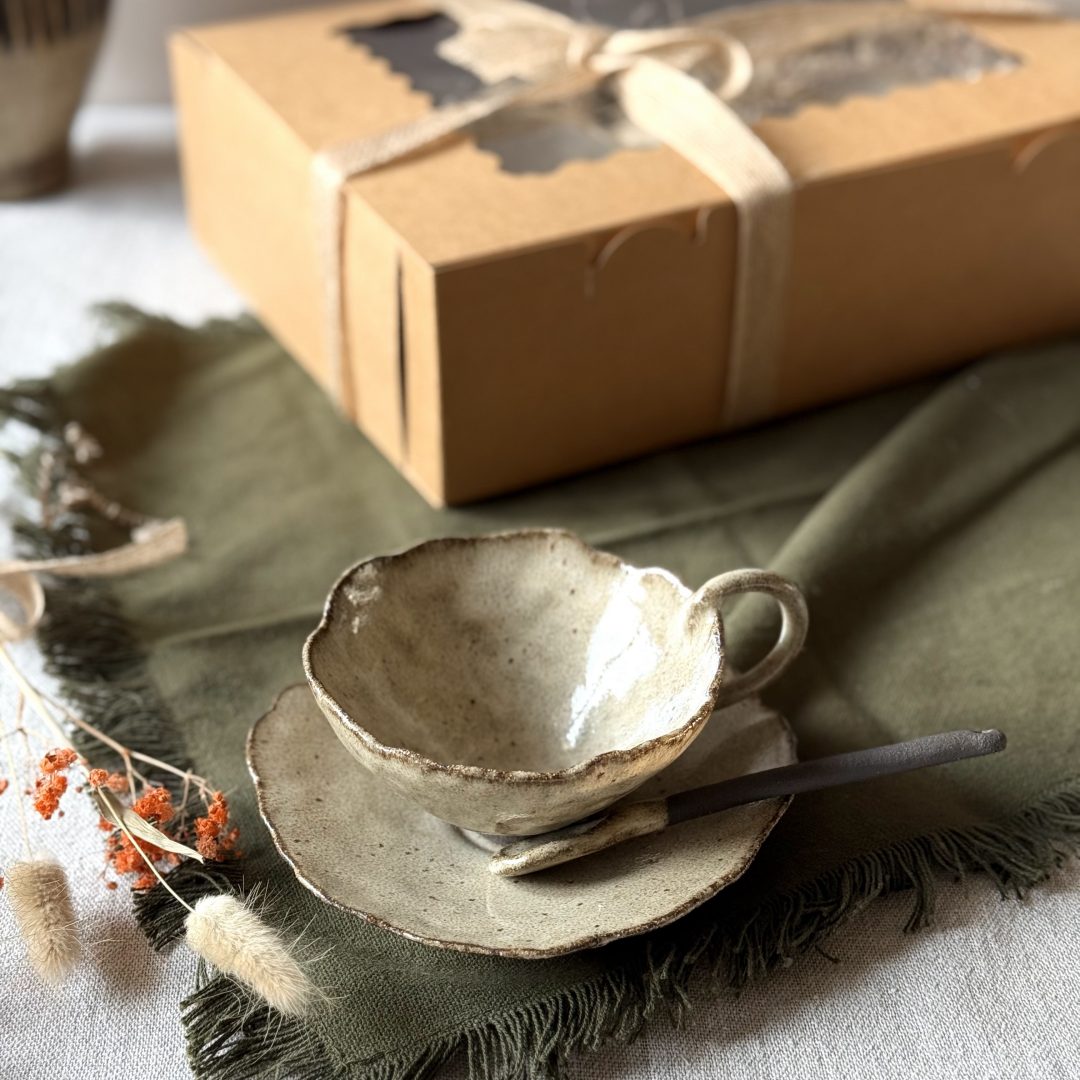 Coffret Lilium posé sur la table, avec la tasse Lilium en grès noir, la sous-tasse Dahlia et la cuillère Rosa présentées au premier plan.