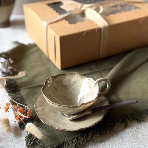 Coffret Lilium posé sur la table, avec la tasse Lilium en grès noir, la sous-tasse Dahlia et la cuillère Rosa présentées au premier plan.