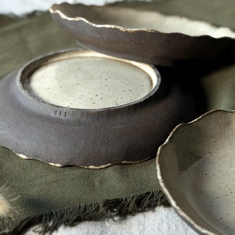 Trois assiettes Jasmina posées sur la table, dont une retournée montrant le pied émaillé, la signature sur le bord et la terre noire visible sur les bords des assiettes.