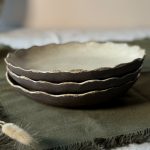 Trois assiettes Jasmina empilées, vues de profil, montrant la terre noire et le bord délicatement émaillé, posées sur une table.