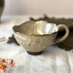 Tasse Aster en grès noir émaillé crème, vue de profil et posée sur une table.