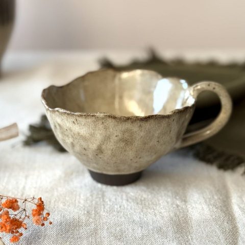 Tasse Aster en grès noir émaillé crème, vue de profil et posée sur une table.