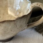 Gros plan sur la tasse Aster montrant la anse, le bord émaillé crème et la base en grès noir.