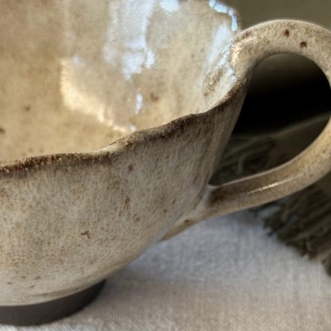Gros plan sur la tasse Aster montrant la anse, le bord émaillé crème et la base en grès noir.