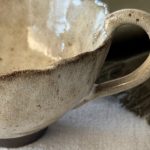 Gros plan sur la tasse Aster montrant la anse, le bord émaillé crème et la base en grès noir.