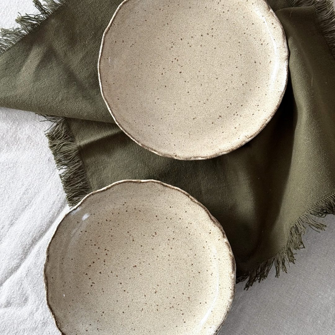 Deux assiettes Jasmina en grès noir vues de dessus, montrant l’émail crème, posées sur une serviette sur la table.