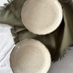 Deux assiettes Jasmina en grès noir vues de dessus, montrant l’émail crème, posées sur une serviette sur la table.