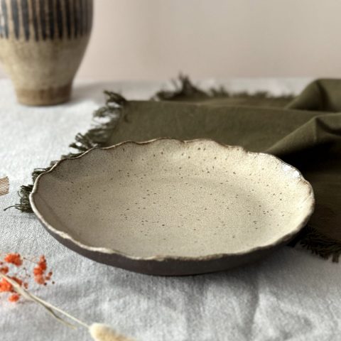 Assiette Jasmina en grès noir, faite main, posée sur une table.