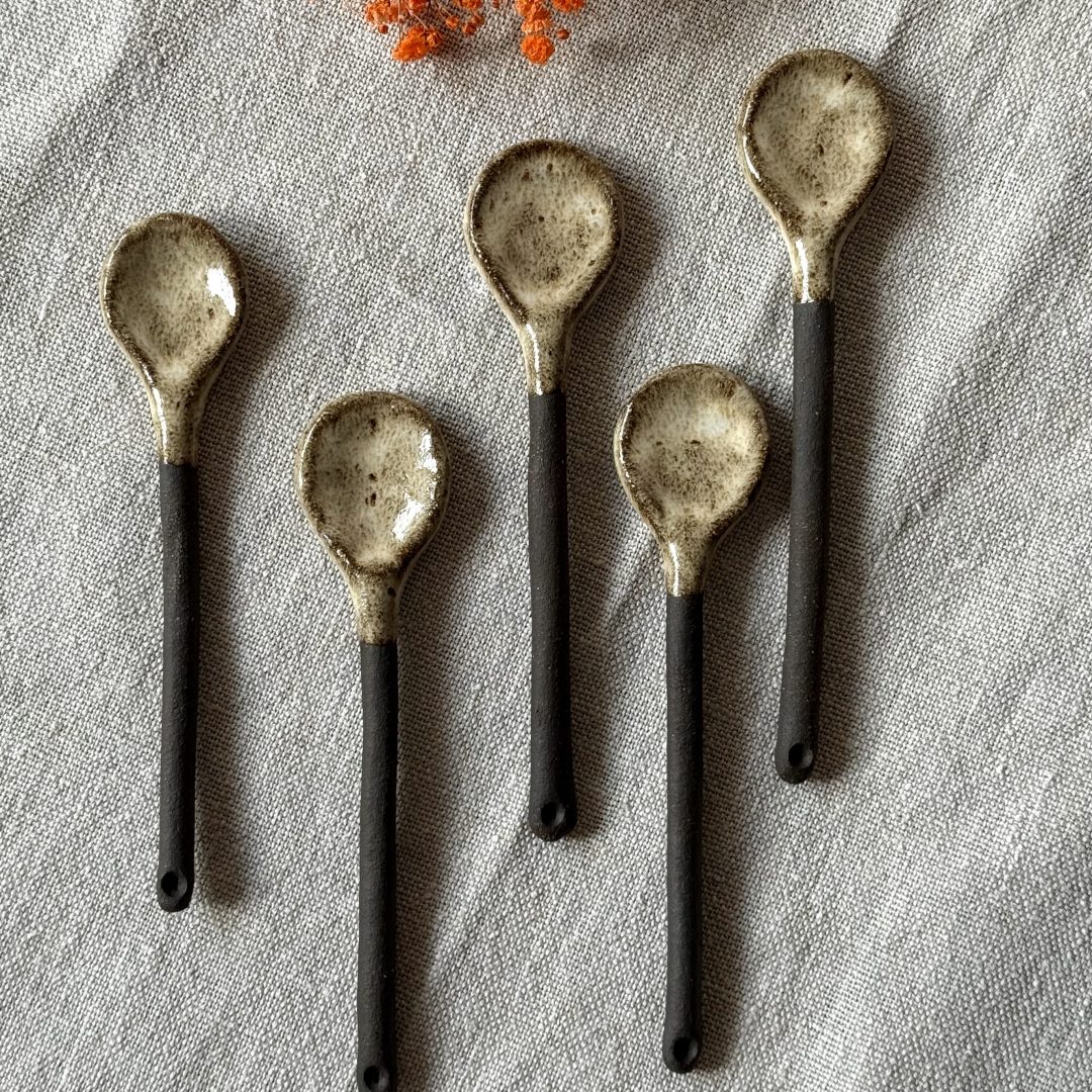 Plusieurs cuillères rosa en céramique artisanale alignées sur une table.