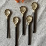 Plusieurs cuillères rosa en céramique artisanale alignées sur une table.