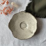 Sous-tasse Dahlia vue de dessus, montrant sa forme ondulée et son renfort central en grès noir émaillé crème.