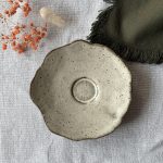 Sous-tasse Dahlia vue de dessus, montrant sa forme ondulée et son renfort central en grès noir émaillé crème.