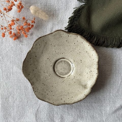 Sous-tasse Dahlia vue de dessus, montrant sa forme ondulée et son renfort central en grès noir émaillé crème.