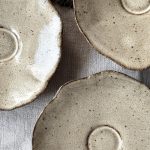 Vue rapprochée de trois sous-tasses Dahlia en céramique artisanale vues de dessus, montrant leur bord ondulé et le renfort central destiné à caler la tasse.