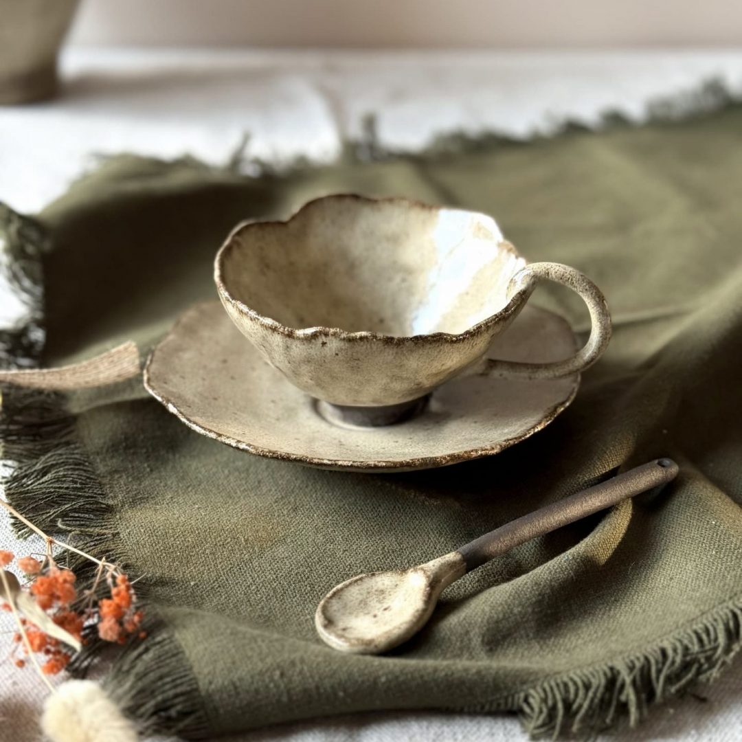 Tasse Lilium en céramique artisanale vue en légère plongée, posée sur la sous-tasse Dahlia avec la cuillère Rosa, sur une table.