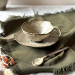 Tasse Lilium en céramique artisanale vue en légère plongée, posée sur la sous-tasse Dahlia avec la cuillère Rosa, sur une table.