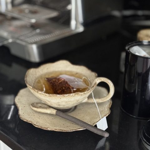 La tasse Lilium en céramique artisanale posée sur la sous-tasse Dahlia avec la cuillère Rosa sur le plan de travail de la cuisine avec un thé.