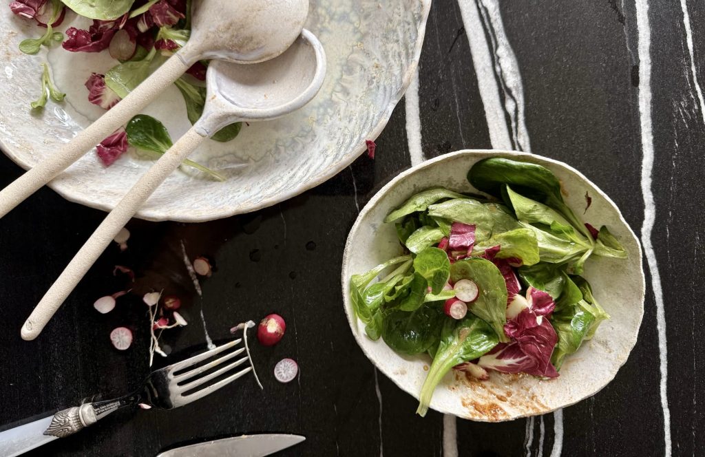 Plat CELESTE avec couverts sur une table avec de la salade et le bol AURORA en grès artisanal avec de la salade.