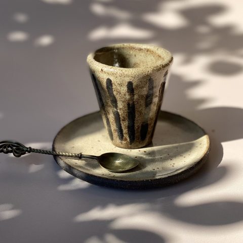 Tasse NAIA en céramique artisanale posée sur sa sous-tasse, fond neutre.