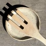 Repose-cuillère en grès noir vue de dessus avec une cuillère en bois dessus.