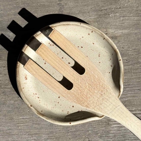 Repose-cuillère en grès noir vue de dessus avec une cuillère en bois dessus.