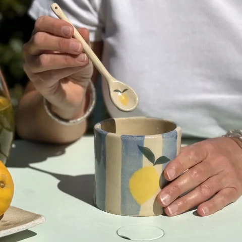 Tasse citron et cuillère en grès blanc sur une table à l'exterieur.