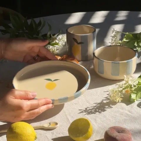 assiette Elia citron entre les mains au dessus d'une table dressée avec la tasse citron et le bol Demba citron en grès artisanal